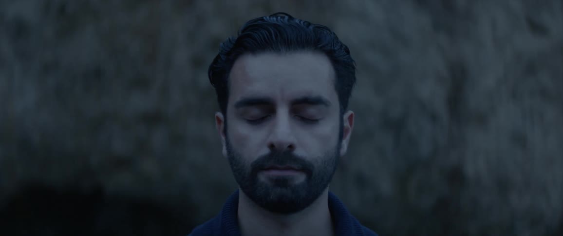 Man standing still outside at dusk closes his eyes