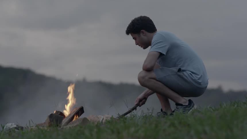 A man puts a stick in a fire on a hill