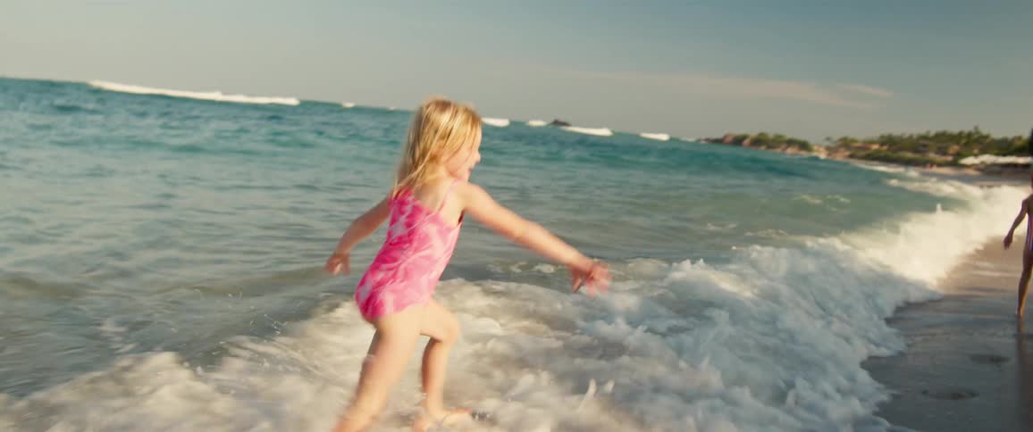 Two young girls are running and playing on a tropical beach