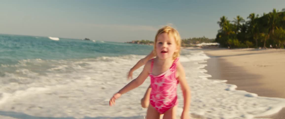 Two young girls running on the beach as waves roll in to shore and over their feet