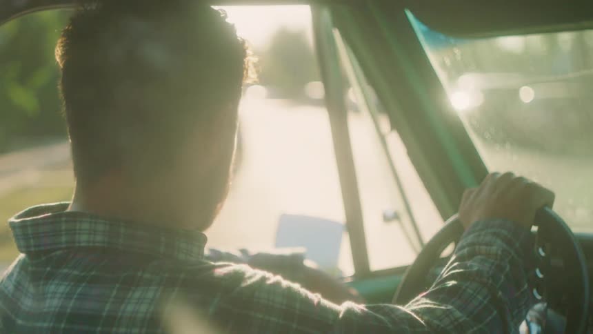 Bearded man steering a vehicle in a city at sunset