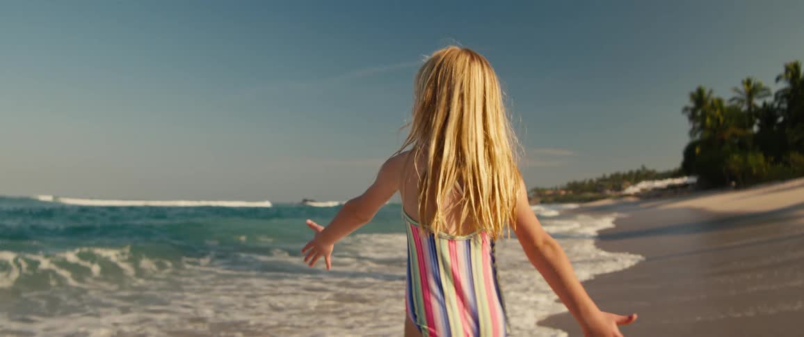 Girl with long hair standing with arms open facing the sea with another child beside her