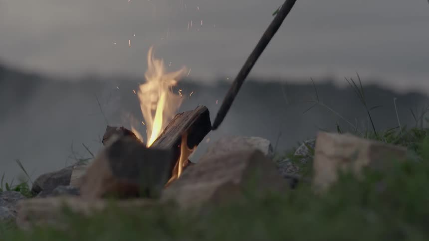 A person pokes a campfire with a stick