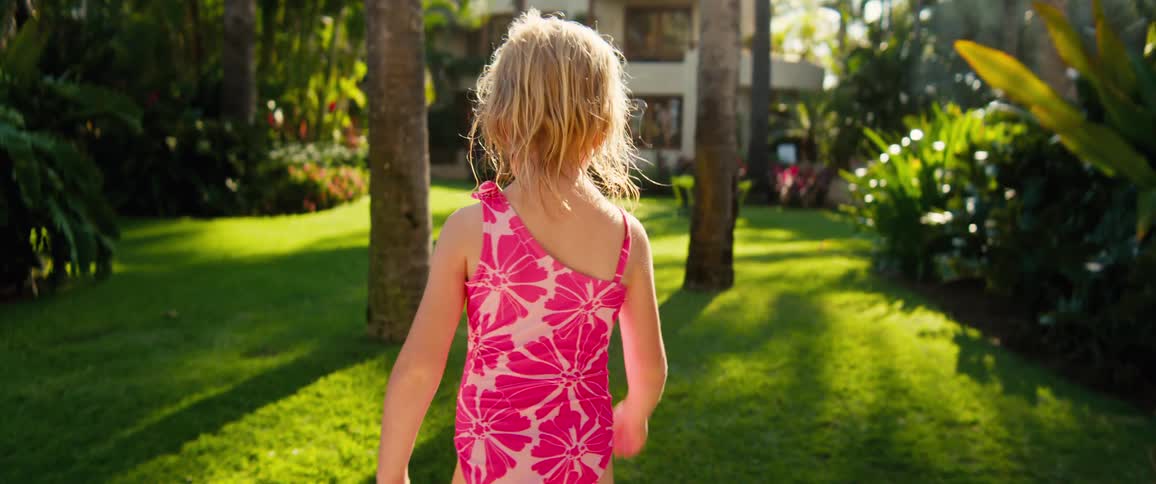 Female child wearing a pink bathing suit walking on the garden of a condo outdoors during day time
