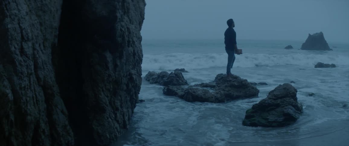 A man standing on the rocks looking out at the ocean