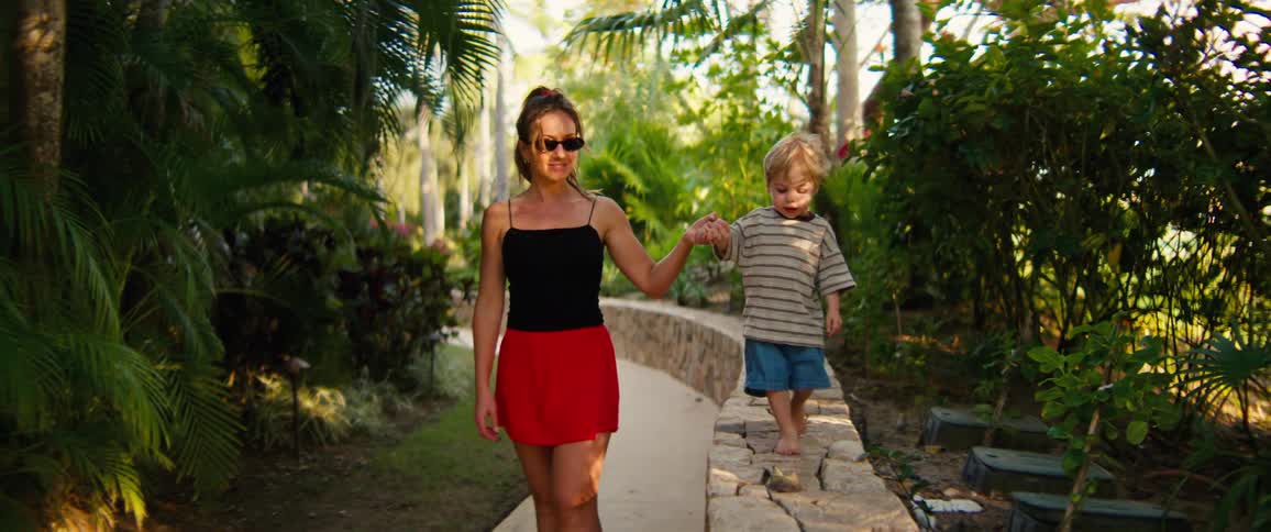 Woman holding a boys hand as he walks on a stone wall in a garden
