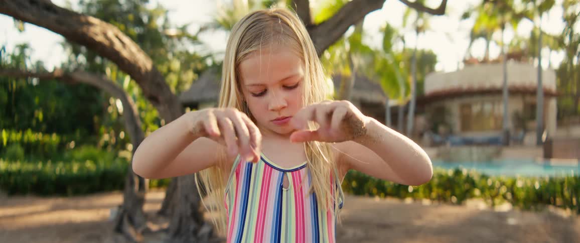 Girl with sand on her raised hands in an outdoor area with trees in the background