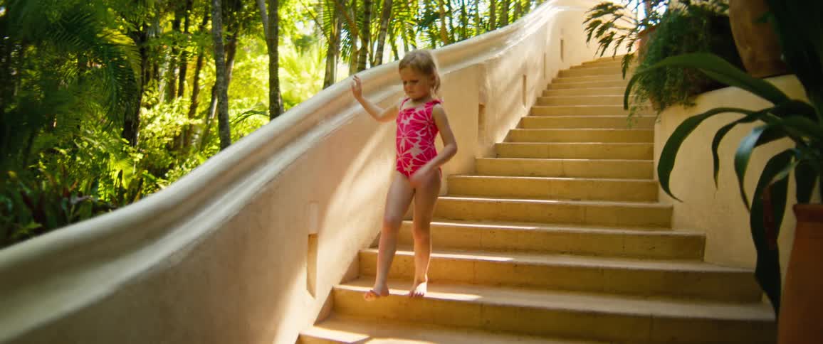 A young girl in a swimsuit descends an outdoor staircase lined with vegetation