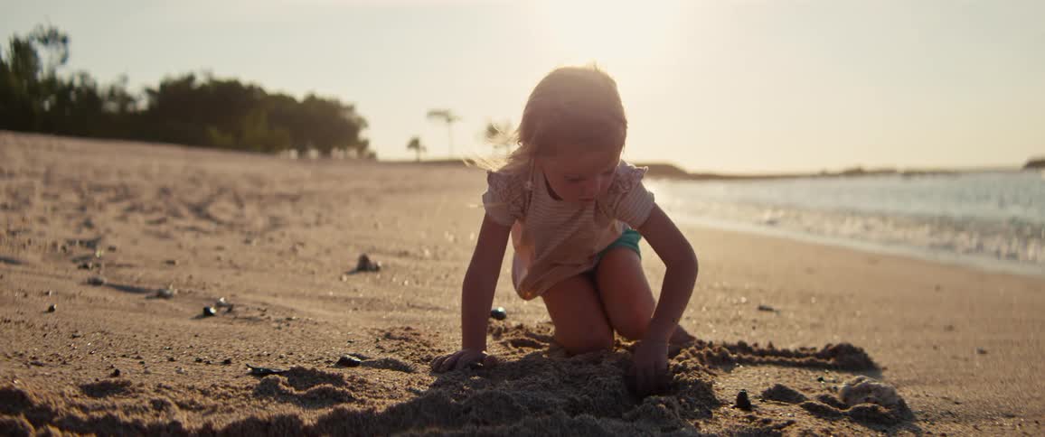 Little girl digging in the sand at the beach as waves roll in to shore and over the sand
