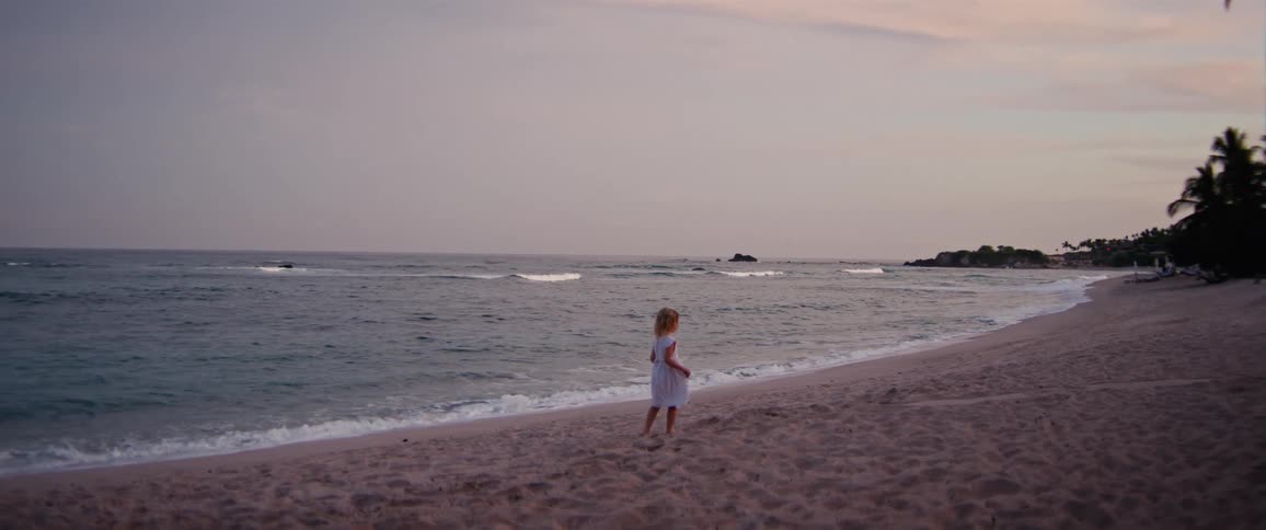Girl walking alone on the beach sand at dusk with the sea beside her
