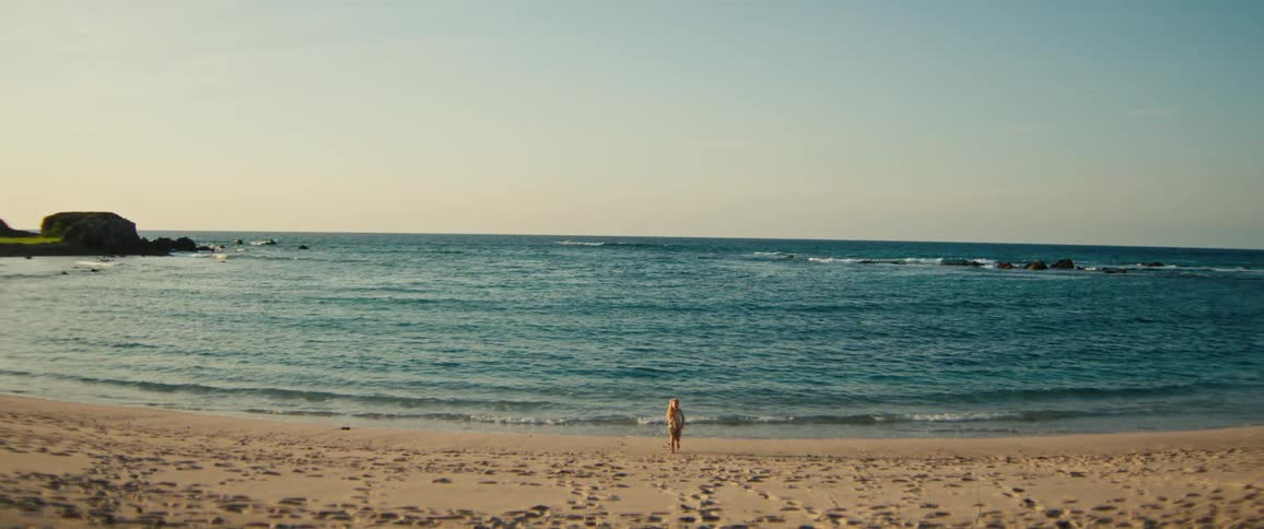 A child runs away from the ocean waves on the sandy beach on a sunny day