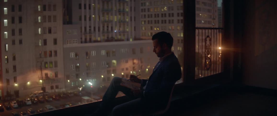 Man sits next a large window looking out at a busy city