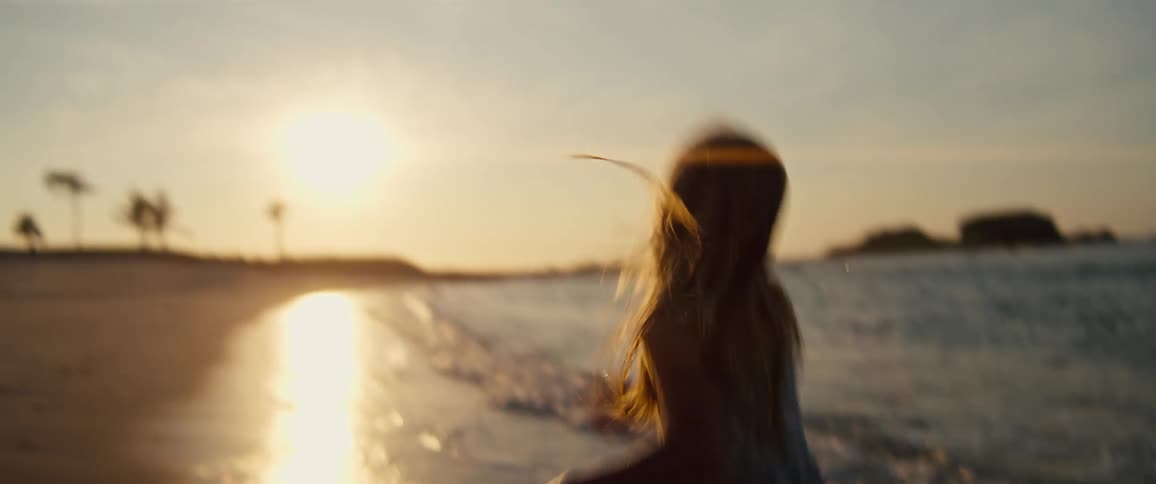 Blonde girl wearing a dress running next to the sea on a beach outdoors during sunset time