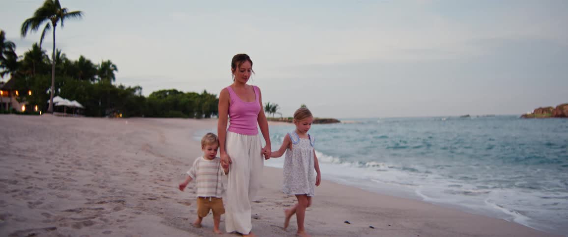 Mother walks and holds hands with her children as they walk on the beach in the early evening