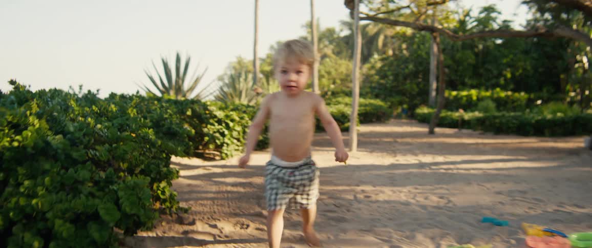 Boy running barefoot in an outdoor area with trees and buildings in the background