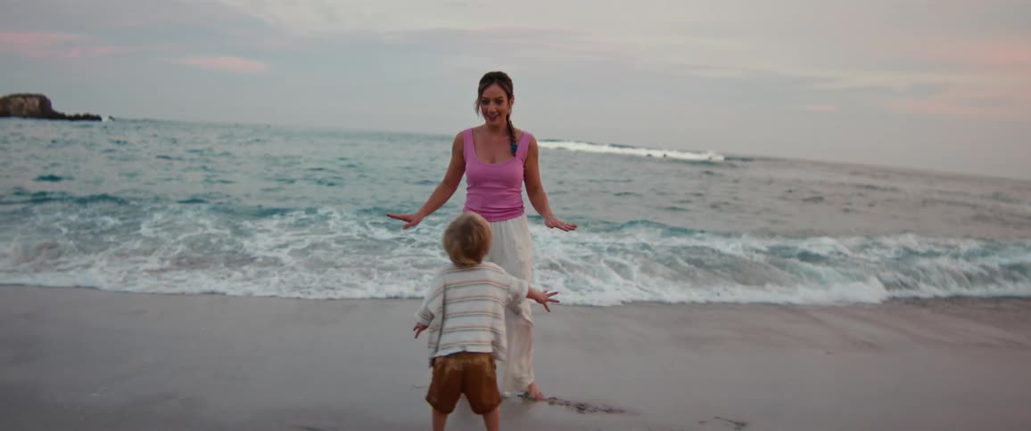 Woman and child standing on the sand facing the sea with waves in the background