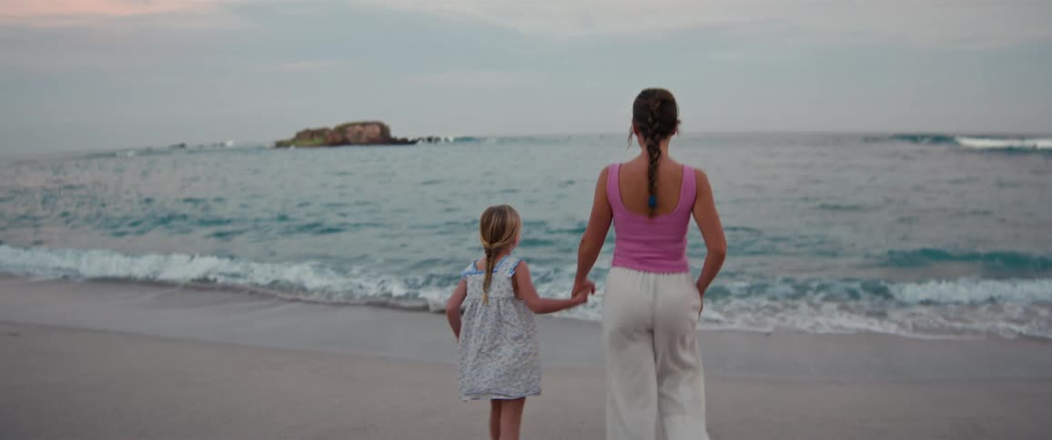 A woman walks with her daughter on the beach towards the ocean