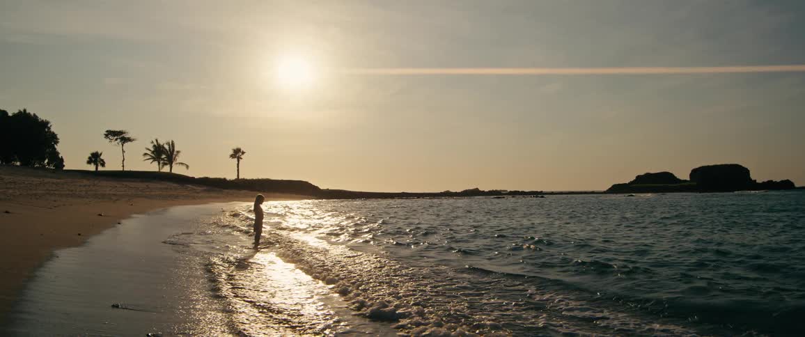 A young girl plays on the beach at sunset running away as the waves touch her feet
