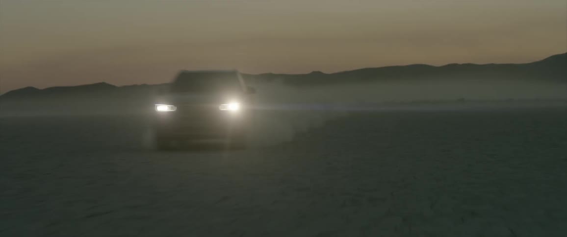 A car passes down the desert and kicks up sand