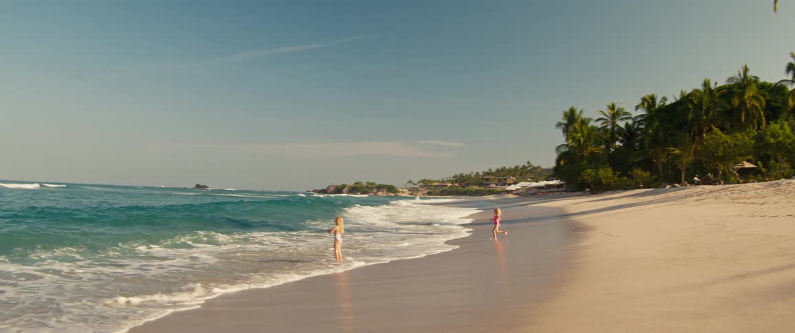 Young girls run into the surf while playing on the beach on a summer day