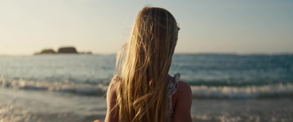 Child in light dress walking on beach toward the sea