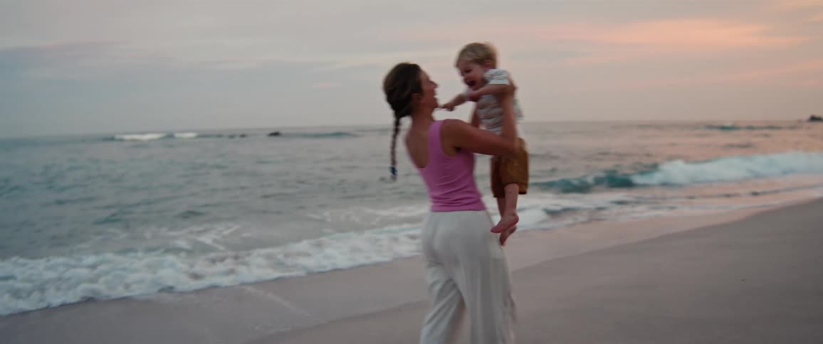 The mother spins her son around on the beach