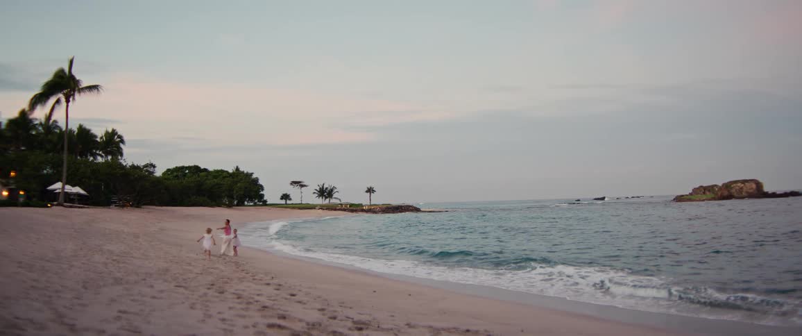 Woman and child running hand in hand along the beach by the sea with palm trees in the background
