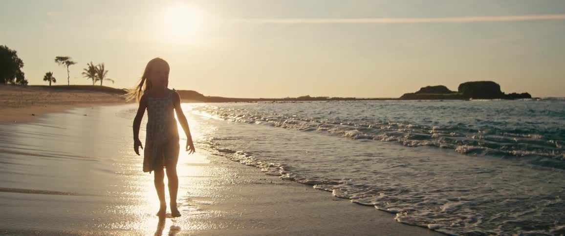Girl walking along the shoreline with low sun reflecting on the water