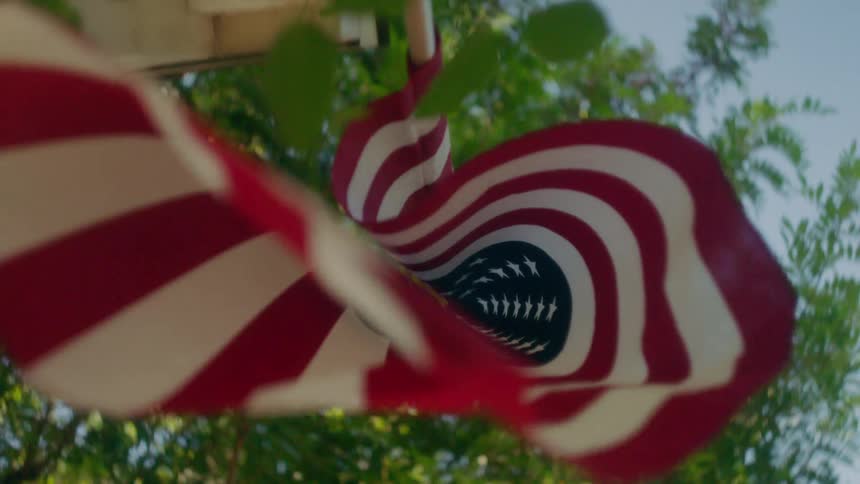 American flag waves in front of a house and trees