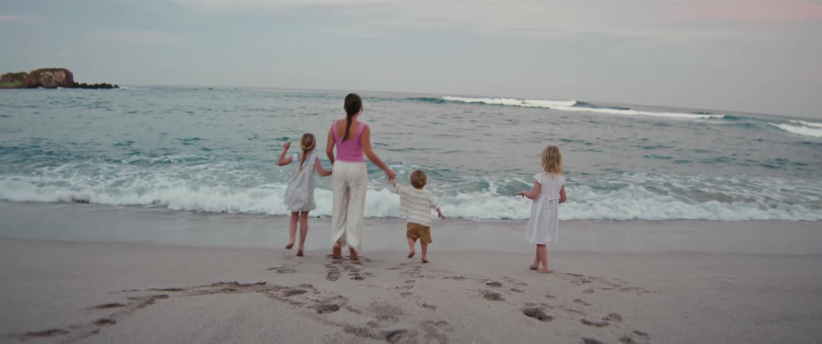 Woman and three children walking hand in hand toward the sea on the beach