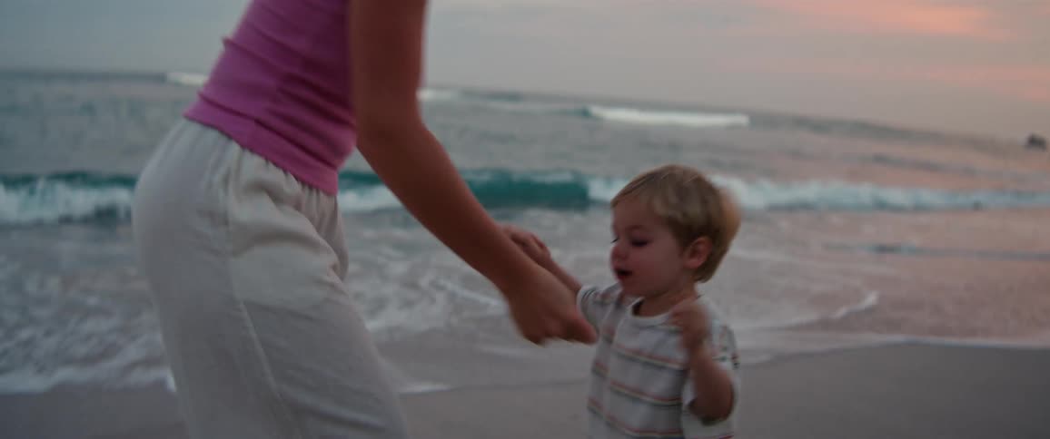 Woman lifting a child into the air on the beach at dusk with the sea in the background