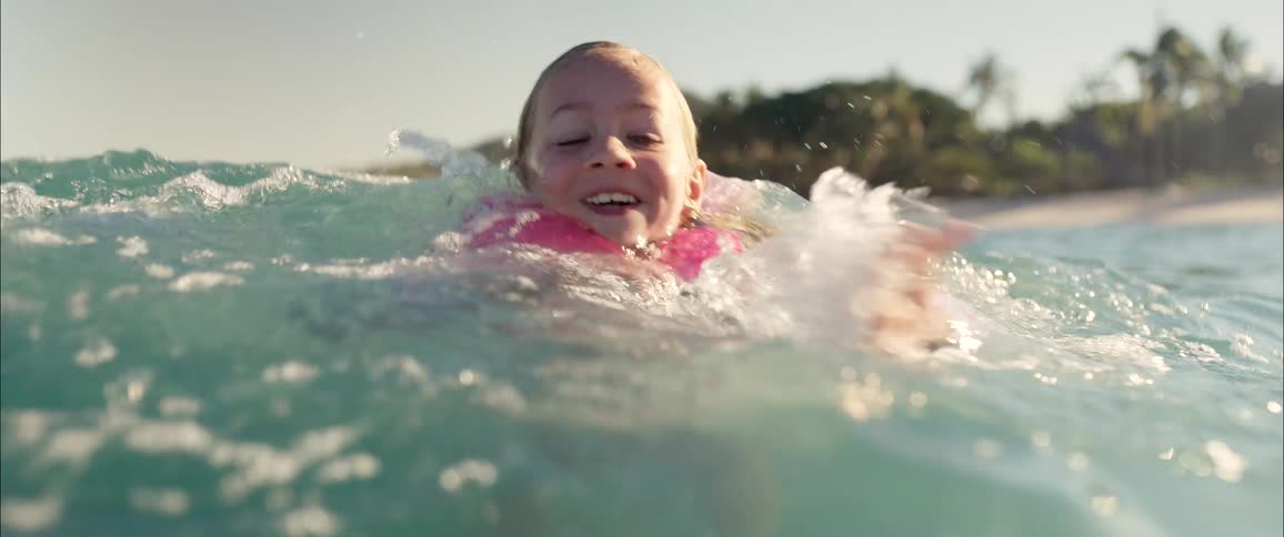 Little girl smiles as she swims in the water wearing a life jacket