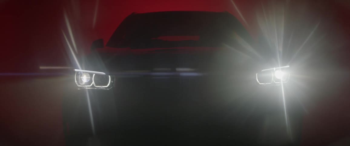 A car with bright headlights is parked inside a dark area with glowing red lighting in the background