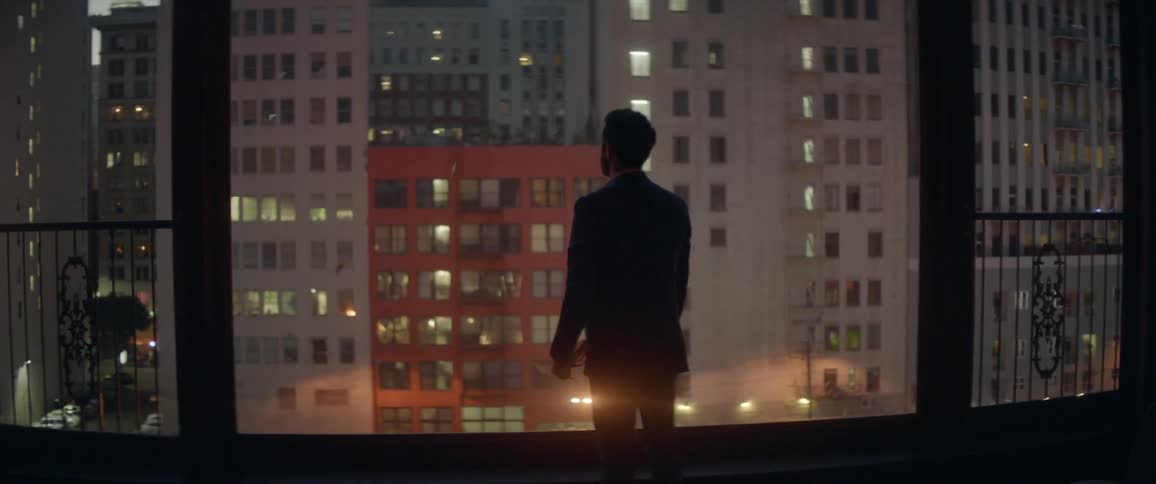 Man looks out a window at skyscrapers at night