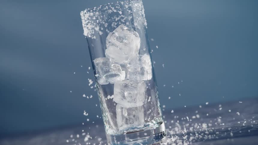 Ice cubes falling into clear glass against blue background