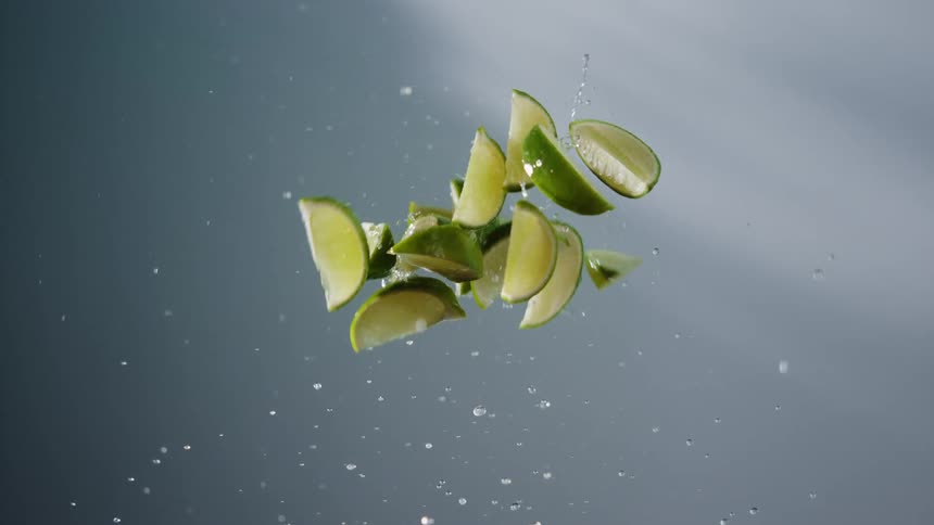 Green lime wedges suspended midair with water droplets against a gray background
