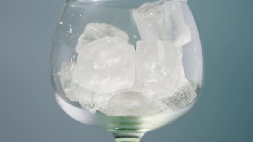 Ice cubes fall into a wine glass against a blue background