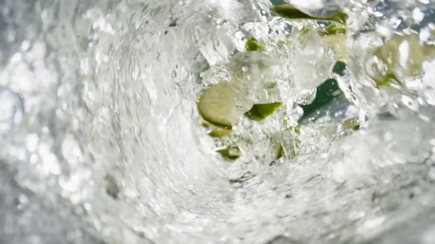 Ice alcohol and apple slices swirl inside a glass as more alcohol is poured into it at midday