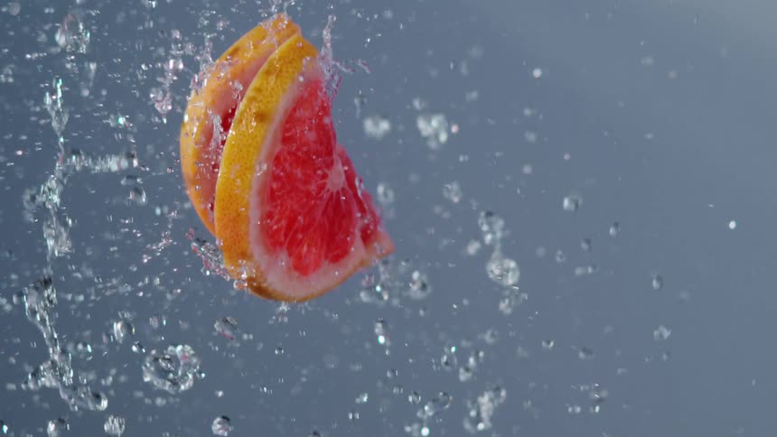 Liquid flying into the air impacts two slices of falling grapefruit