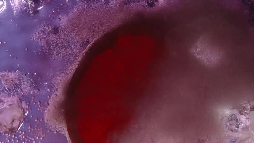 Grapefruit slice submerged in liquid with bubbles and ice around it