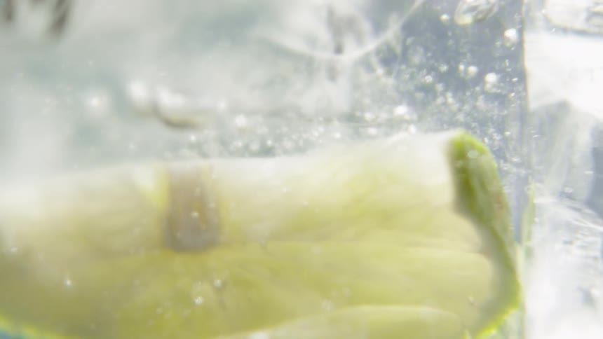 A view inside a rotating glass shows clear liquid ice cubes and lime slices swirling together to create a refreshing drink with a dynamic effect