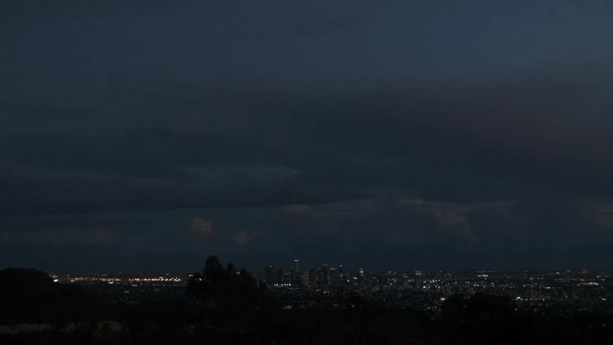 A distant city skyline under a dark and heavy cloud cover during twilight and night