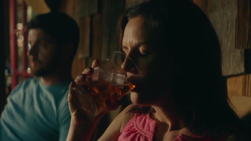 Woman sipping from an iced drink while sitting indoors next to a man