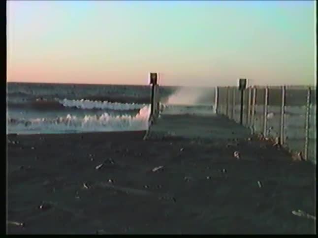 Beach with waves breaking beside wooden structure extending into the sea under clear sky