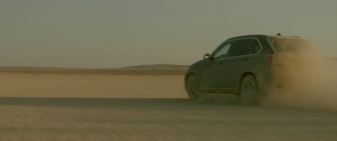 A car drives through the desert kicking up dust