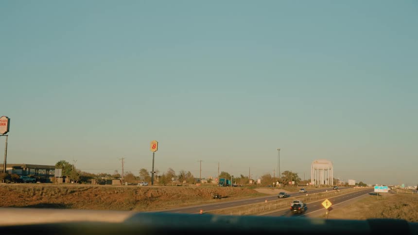 Traffic moving along a highway crosses under a bridge in a town during the daytime