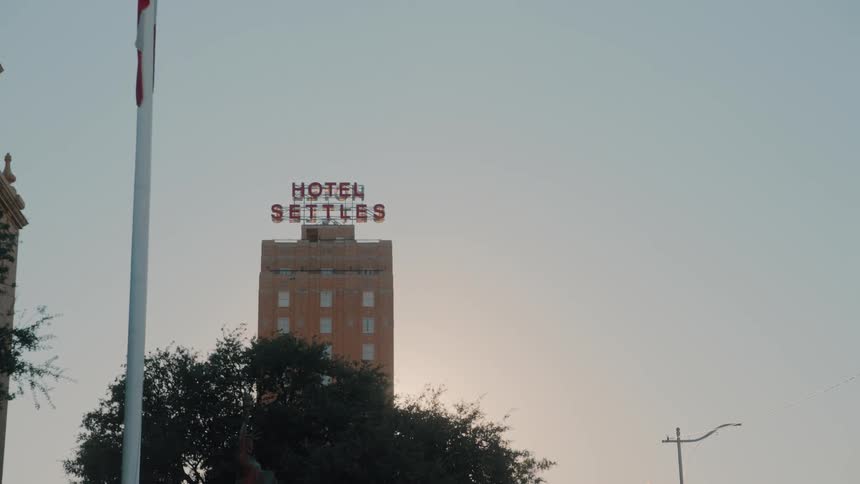 The video shows a tall historic brick building with a large neon sign on its roof the sign reads hotel settles in glowing red letters against a pale evening sky