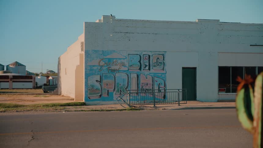 White car in motion in front of building with painted mural on the facade