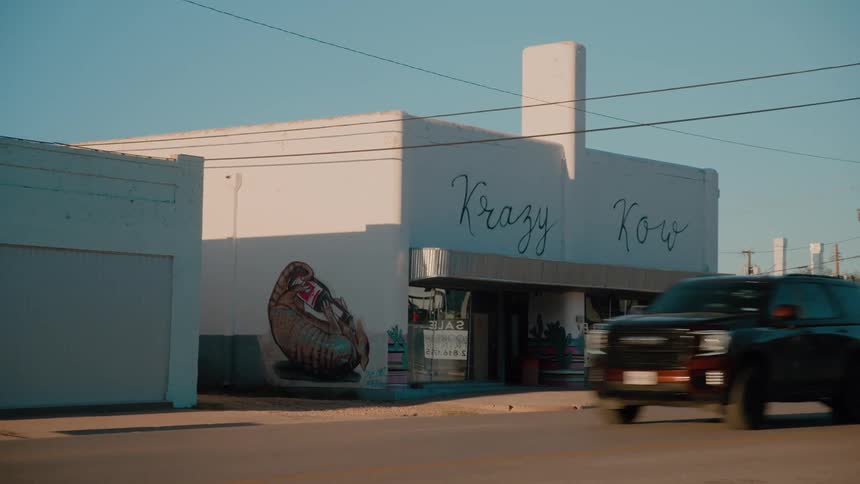 A street view shows a for sale sign in front of a building as an suv drives down the street on a sunny day