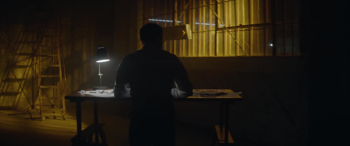 Man works at a desk with one dim lamp